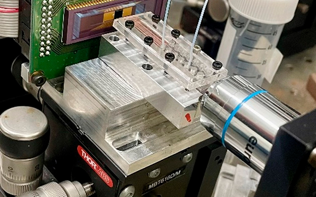 Close-up of a laboratory microfluidic testing device with tubing and a syringe.