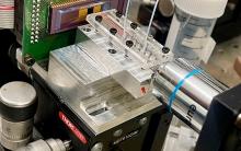 Close-up of a laboratory microfluidic testing device with tubing and a syringe.