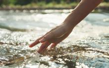 Close-up of woman's hand touching water in the river
